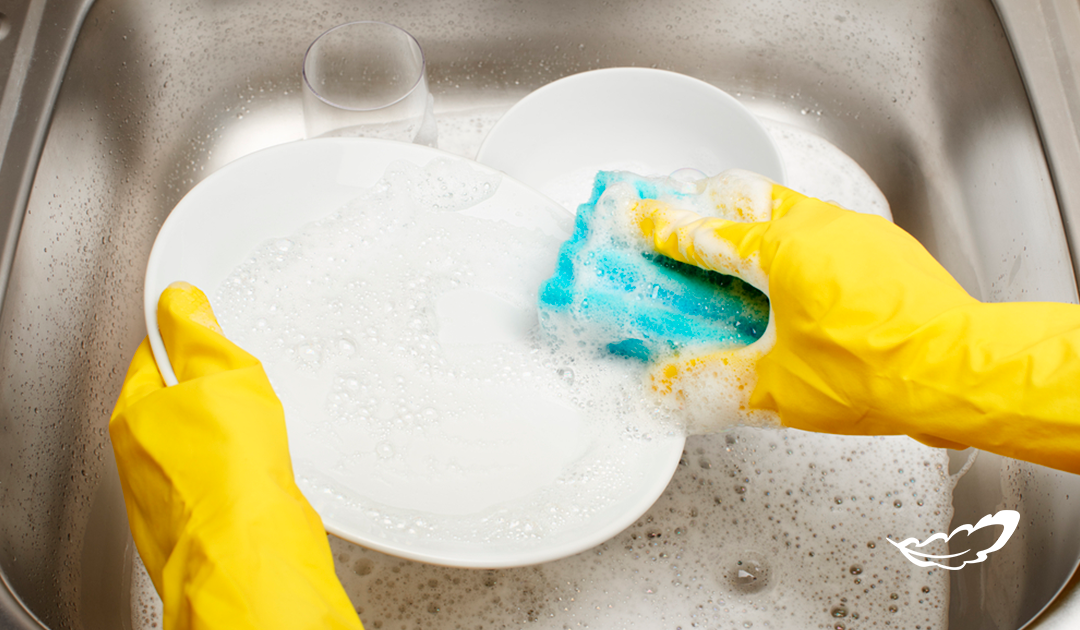 Detergente neutro - na imagem possui duas mãos com luvas amarelas lavando um prato branco na pia.